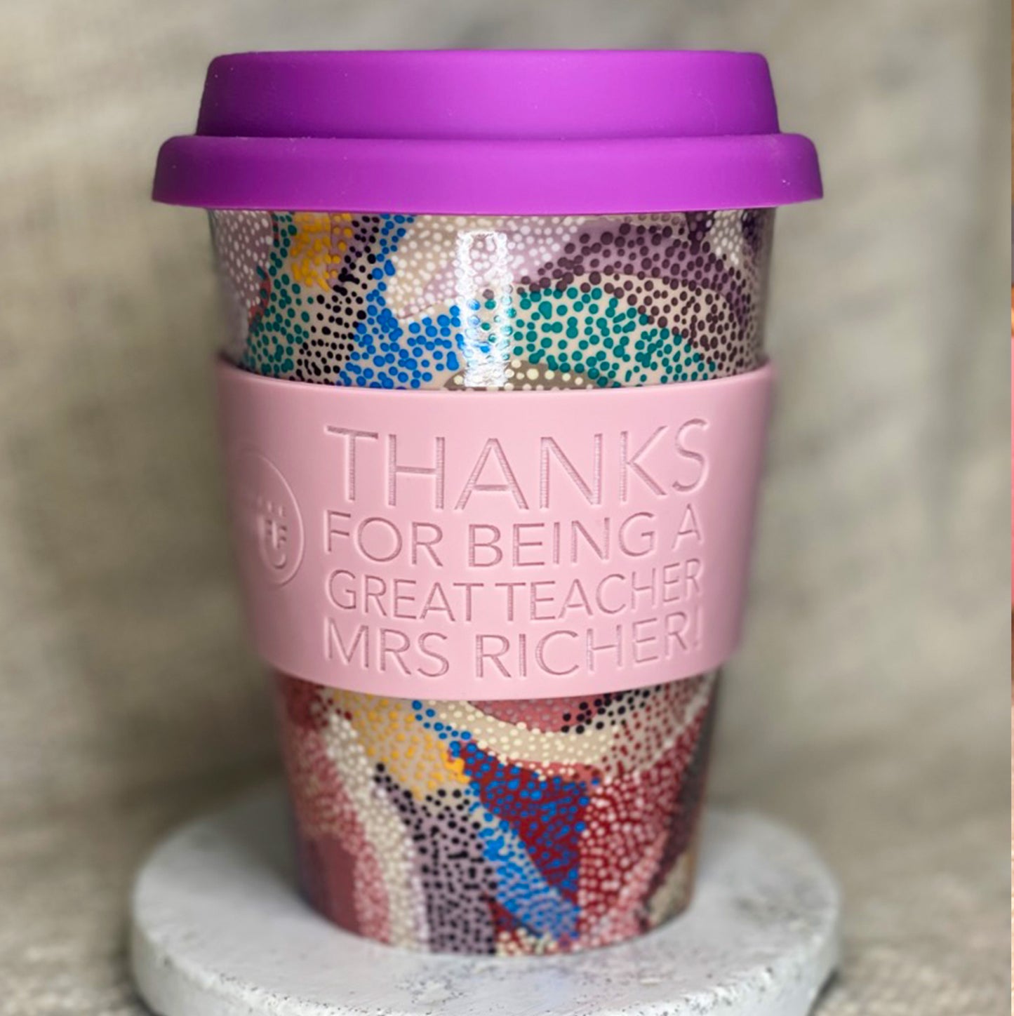 Colorful patterned cup with a pink sleeve and purple lid on a neutral background