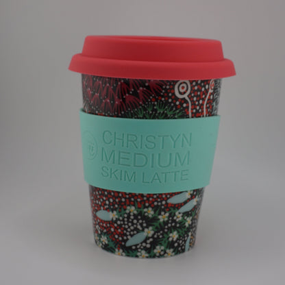 A reusable coffee cup with a red lid and a turquoise sleeve printed with the text 'CHRISTYN MEDIUM SKIM LATTE', set against a plain light gray background.