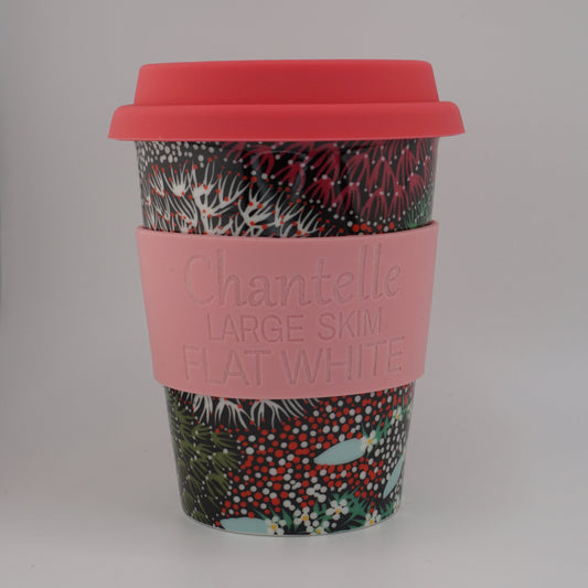 A reusable travel tumbler with a coral red lid, a pink silicone sleeve embossed with the brand name 'Charitelle', and a green and red botanical patterned body, shown on a neutral light gray background.